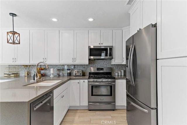 kitchen featuring appliances with stainless steel finishes, decorative light fixtures, white cabinetry, sink, and light hardwood / wood-style flooring