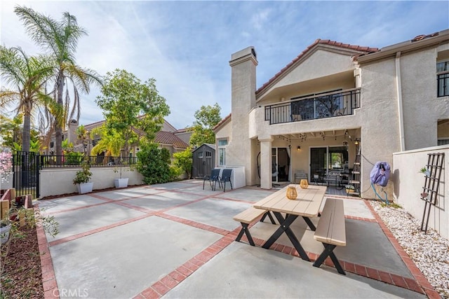 rear view of property with a balcony, a storage unit, and a patio area