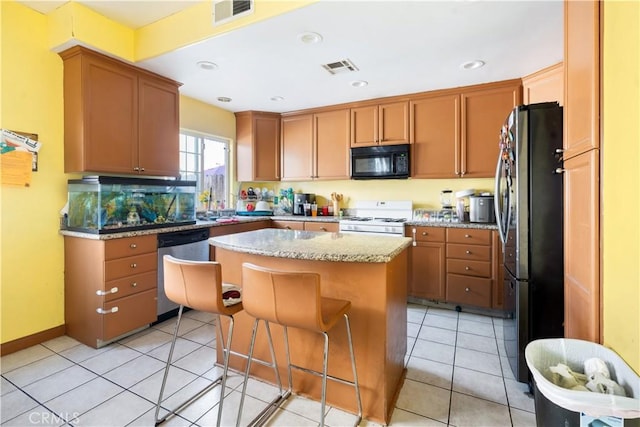 kitchen featuring a breakfast bar area, stainless steel appliances, a center island, light stone countertops, and light tile patterned flooring