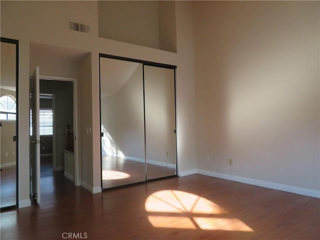 unfurnished bedroom with dark wood-type flooring, a towering ceiling, and a closet