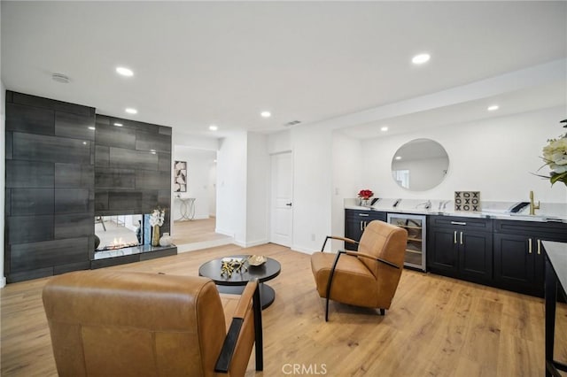 living room featuring bar area, beverage cooler, light hardwood / wood-style floors, and a tile fireplace