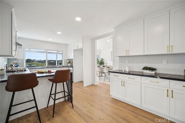 kitchen featuring a kitchen bar, light wood-type flooring, decorative backsplash, and white cabinets