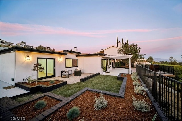 back house at dusk featuring a pergola, a patio, and a lawn