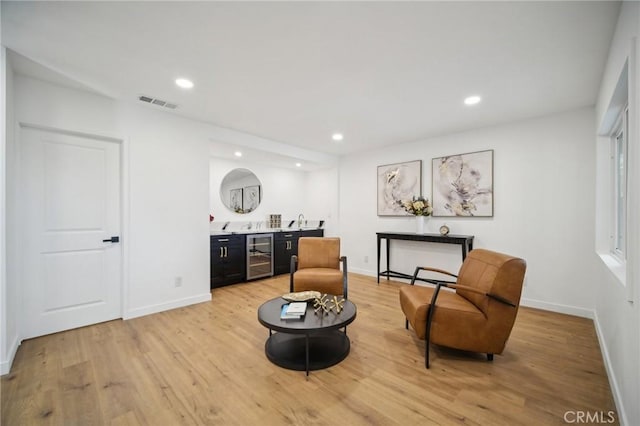 sitting room featuring wine cooler, indoor bar, and light hardwood / wood-style flooring