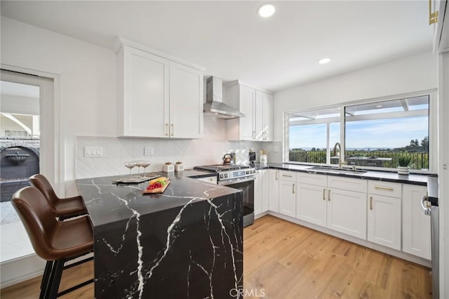 kitchen featuring stainless steel gas stove, sink, white cabinets, kitchen peninsula, and wall chimney exhaust hood