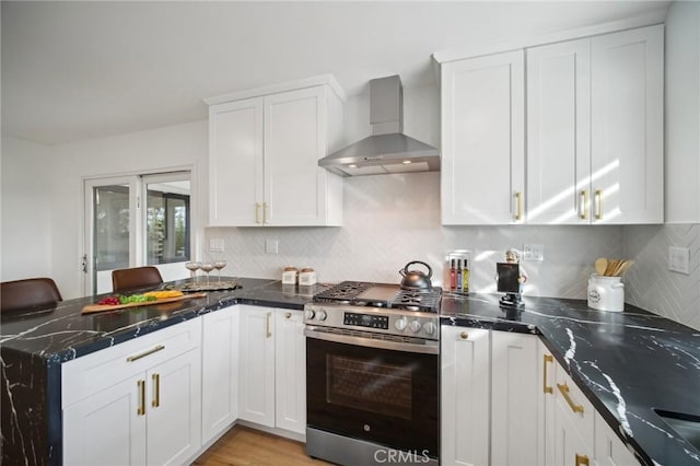 kitchen featuring tasteful backsplash, gas range, wall chimney range hood, and white cabinets