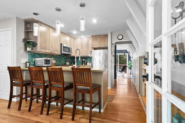 kitchen with hanging light fixtures, stainless steel appliances, light hardwood / wood-style floors, and light brown cabinets