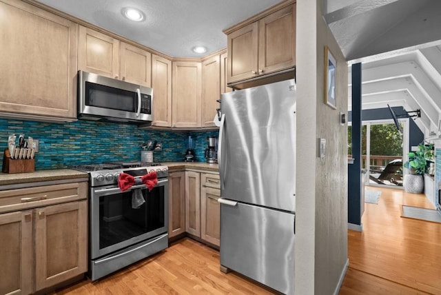 kitchen featuring appliances with stainless steel finishes, tasteful backsplash, light brown cabinetry, vaulted ceiling, and light wood-type flooring