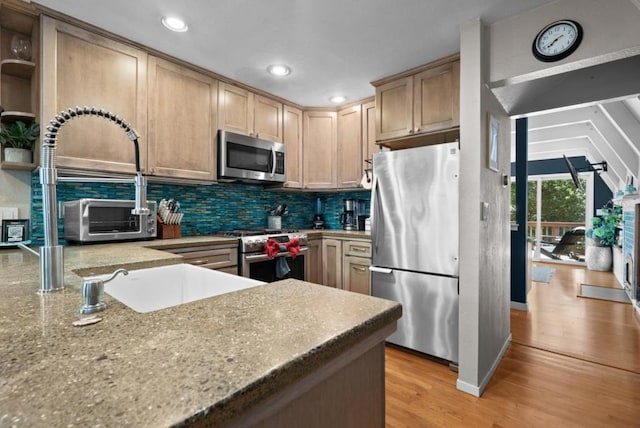 kitchen with light hardwood / wood-style flooring, appliances with stainless steel finishes, backsplash, light stone countertops, and light brown cabinets