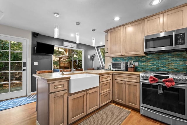 kitchen featuring stainless steel appliances, hanging light fixtures, light hardwood / wood-style flooring, and kitchen peninsula