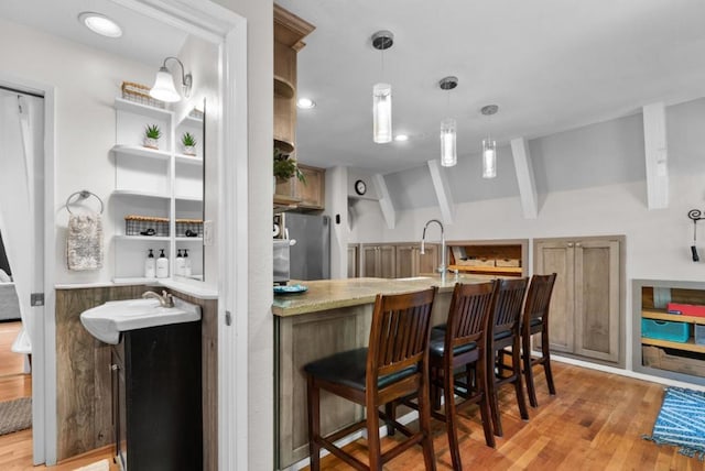 interior space with stainless steel refrigerator, sink, a kitchen bar, light hardwood / wood-style floors, and kitchen peninsula