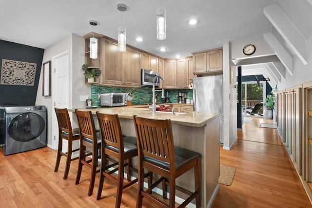 kitchen with pendant lighting, stainless steel appliances, light hardwood / wood-style floors, and backsplash