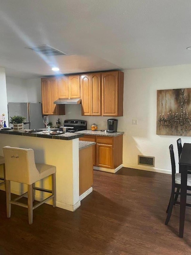 kitchen featuring a breakfast bar area, electric range oven, stainless steel fridge, dark hardwood / wood-style floors, and kitchen peninsula