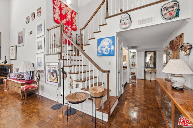 stairway with crown molding, a towering ceiling, and parquet floors