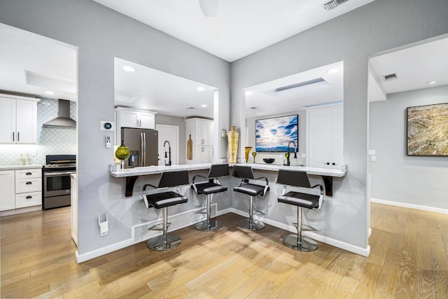 kitchen with wall chimney range hood, white cabinetry, stainless steel appliances, a kitchen breakfast bar, and tasteful backsplash