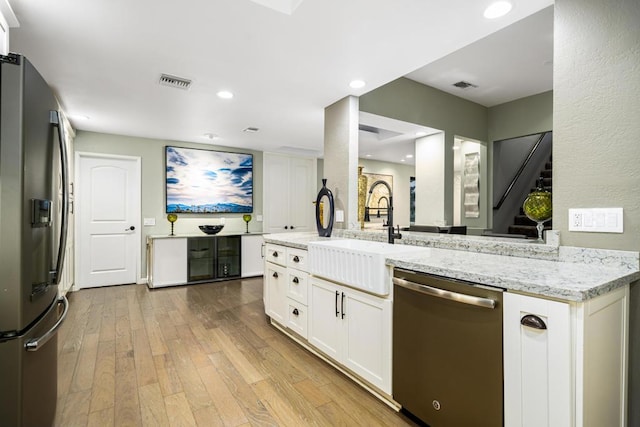 kitchen with sink, appliances with stainless steel finishes, light stone countertops, white cabinets, and kitchen peninsula