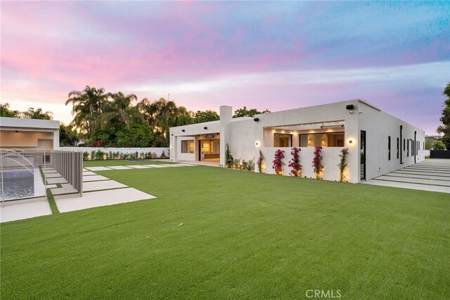 back house at dusk featuring a lawn and a patio