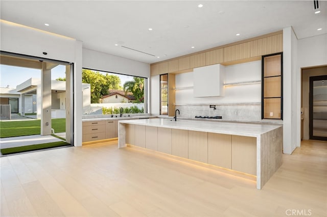 kitchen with sink, light hardwood / wood-style flooring, light brown cabinets, a large island, and light stone countertops