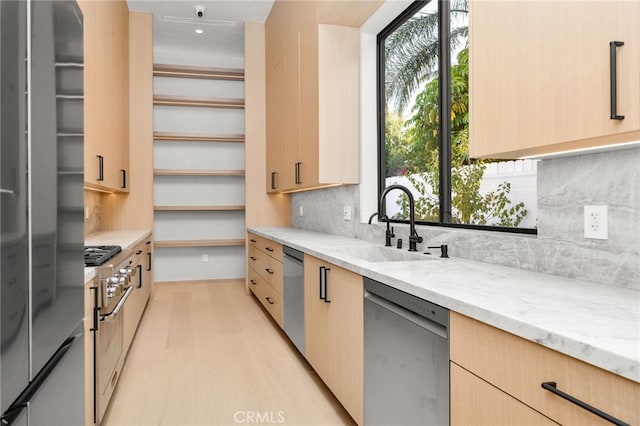 kitchen with light brown cabinetry, sink, light stone counters, light wood-type flooring, and stainless steel appliances