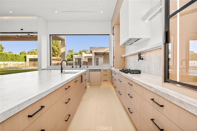 kitchen with light brown cabinetry, sink, stainless steel dishwasher, gas stovetop, and light wood-type flooring