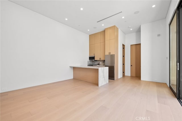 kitchen featuring a kitchen bar, light brown cabinets, kitchen peninsula, light hardwood / wood-style floors, and decorative backsplash