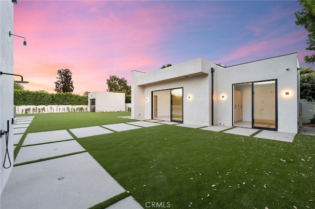 back house at dusk with a yard and a patio