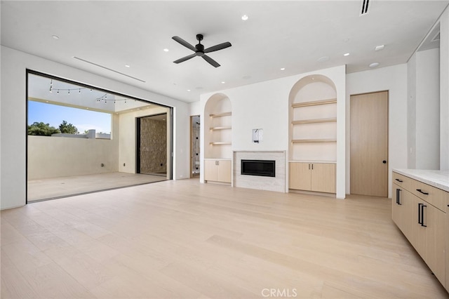 unfurnished living room with ceiling fan, built in features, and light wood-type flooring