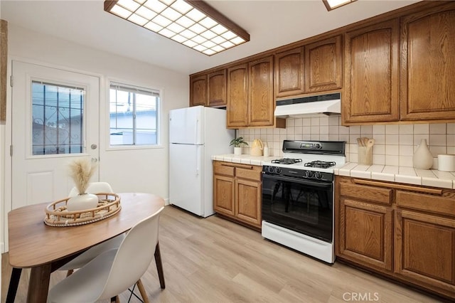 kitchen with white refrigerator, decorative backsplash, range with gas cooktop, and light hardwood / wood-style flooring