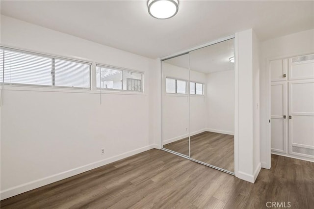 unfurnished bedroom featuring hardwood / wood-style flooring, multiple windows, and a closet