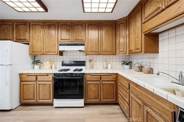 kitchen featuring tasteful backsplash, white fridge, tile counters, light hardwood / wood-style floors, and gas stove