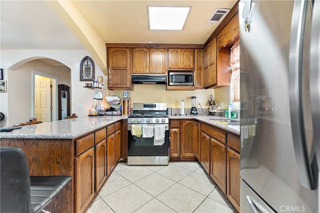 kitchen featuring stainless steel appliances, light tile patterned floors, light stone counters, and range hood