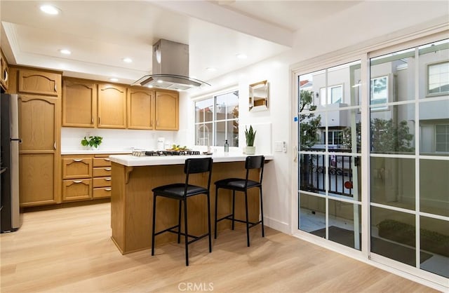 kitchen with a breakfast bar area, island exhaust hood, white gas cooktop, kitchen peninsula, and light wood-type flooring