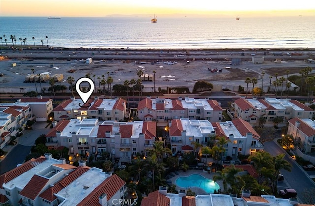 aerial view at dusk featuring a water view and a beach view