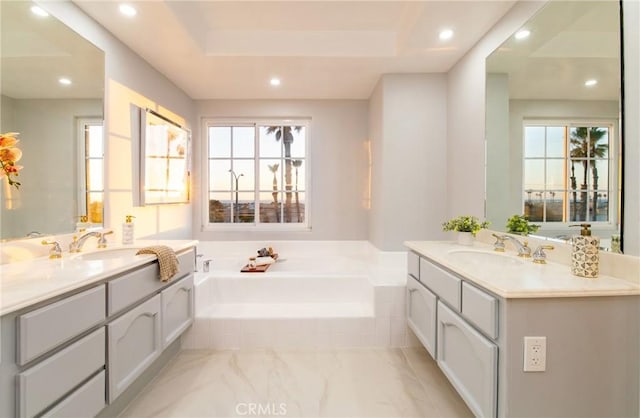 bathroom with vanity, a relaxing tiled tub, and a healthy amount of sunlight