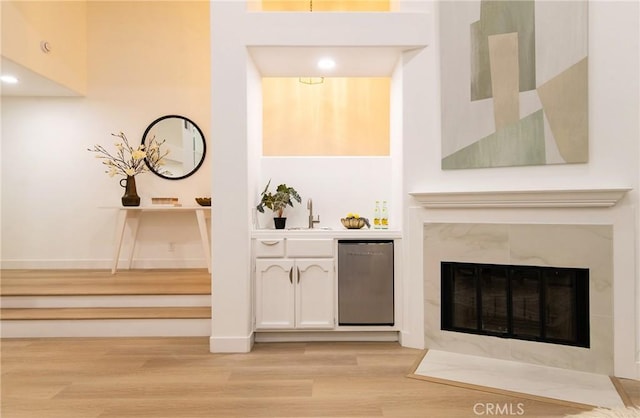 bar featuring sink, light hardwood / wood-style flooring, fridge, white cabinets, and a tiled fireplace