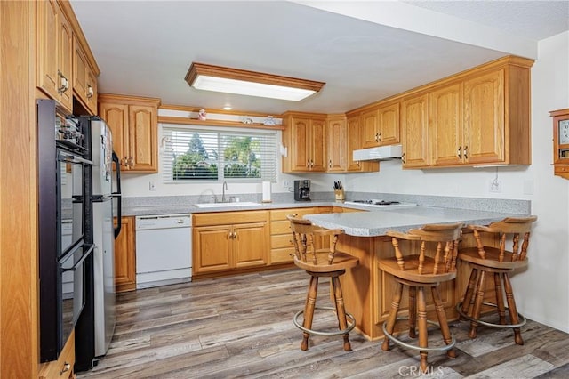 kitchen featuring sink, a kitchen bar, hardwood / wood-style flooring, kitchen peninsula, and white appliances