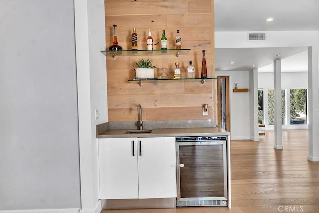 bar with white cabinetry, sink, wine cooler, and light hardwood / wood-style flooring