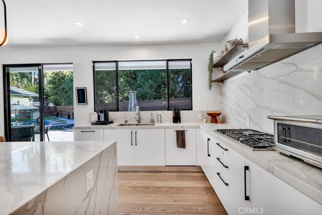 kitchen featuring white cabinetry, island exhaust hood, light stone countertops, and sink