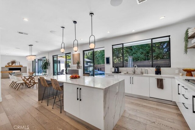 kitchen featuring sink, white cabinetry, decorative light fixtures, a kitchen island, and light hardwood / wood-style floors