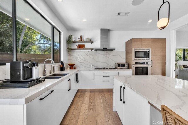 kitchen featuring appliances with stainless steel finishes, tasteful backsplash, white cabinetry, sink, and wall chimney range hood