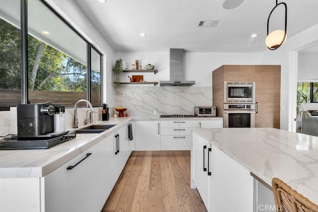 kitchen with appliances with stainless steel finishes, decorative light fixtures, white cabinetry, sink, and wall chimney range hood