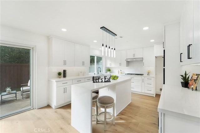 kitchen featuring a kitchen island, a breakfast bar, pendant lighting, white cabinets, and light hardwood / wood-style floors