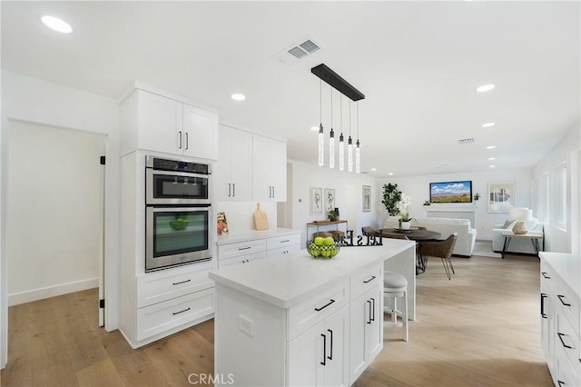 kitchen with light hardwood / wood-style flooring, white cabinets, a kitchen island, decorative light fixtures, and stainless steel double oven