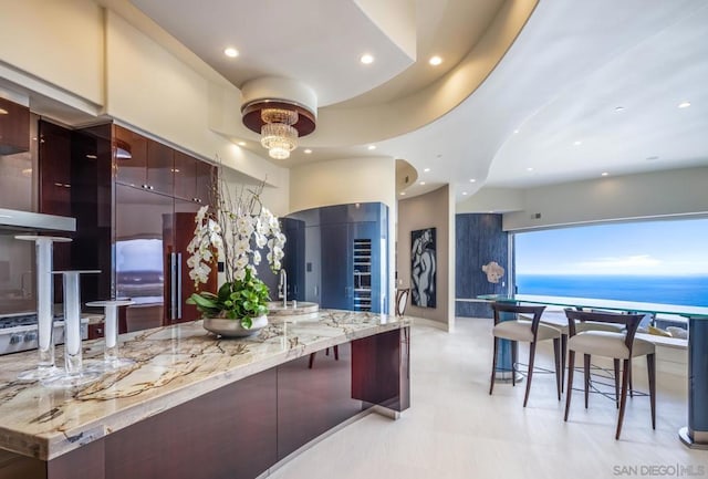 kitchen with light stone counters, a kitchen breakfast bar, a chandelier, and a water view