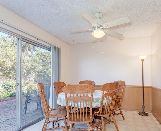 dining area featuring ceiling fan, wooden walls, and a textured ceiling