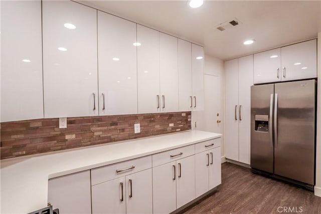 kitchen with stainless steel refrigerator with ice dispenser, dark hardwood / wood-style floors, white cabinets, and backsplash