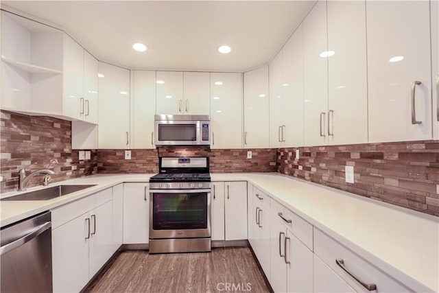 kitchen featuring sink, appliances with stainless steel finishes, hardwood / wood-style flooring, decorative backsplash, and white cabinets