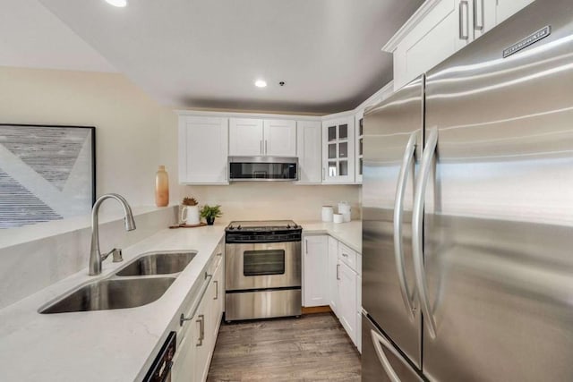 kitchen with sink, dark wood-type flooring, appliances with stainless steel finishes, light stone counters, and white cabinets