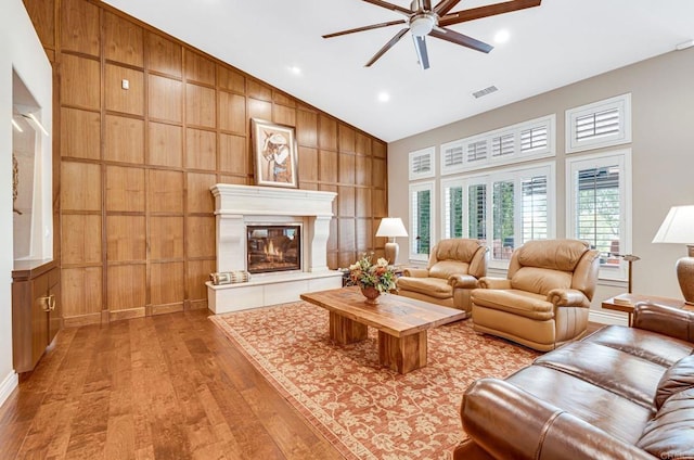 living room with ceiling fan, vaulted ceiling, light hardwood / wood-style flooring, and wood walls