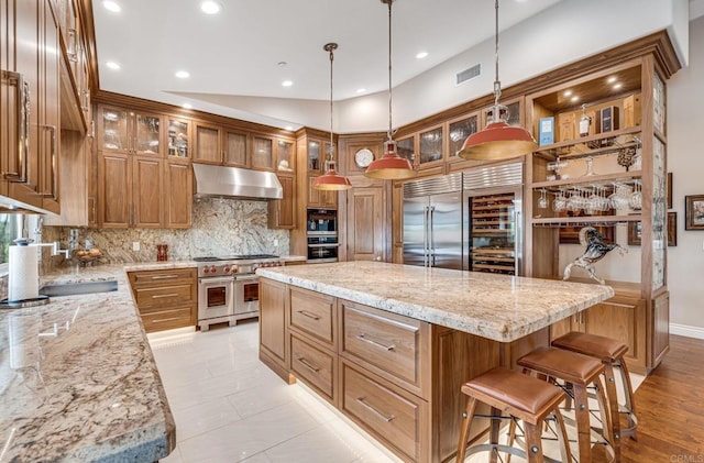 kitchen with high quality appliances, light stone countertops, a kitchen island, and pendant lighting